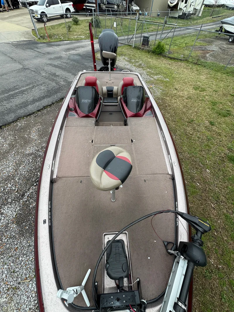 Slide: The Image of 2012 Skeeter ZX 21 fishing boat with red and gray seating, parked on gravel. - 2