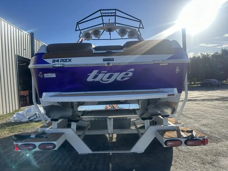 Slide: The Image of 2025 Tigé 24RZX boat, rear view, purple hull, parked outdoors in sunlight. - 6