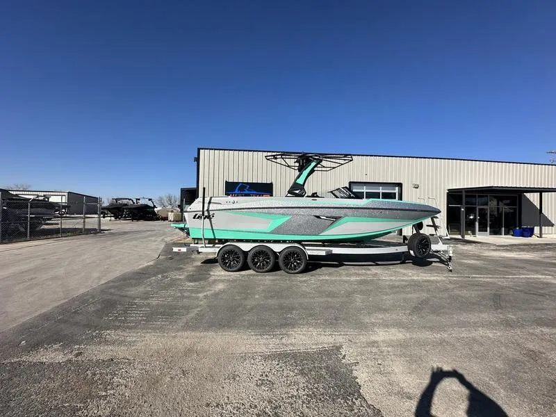Slide: The Image of 2025 Tigé 24RZX boat on trailer, parked outside a warehouse under clear blue sky. - 0