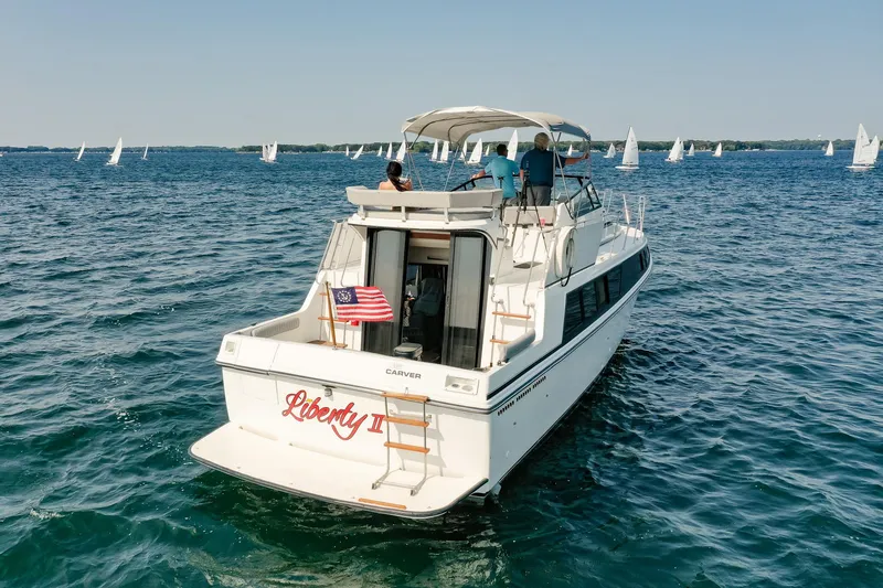 Slide: The Image of 1987 Carver 3697 Mariner yacht on open water, with people onboard and sailboats in the background. - 4