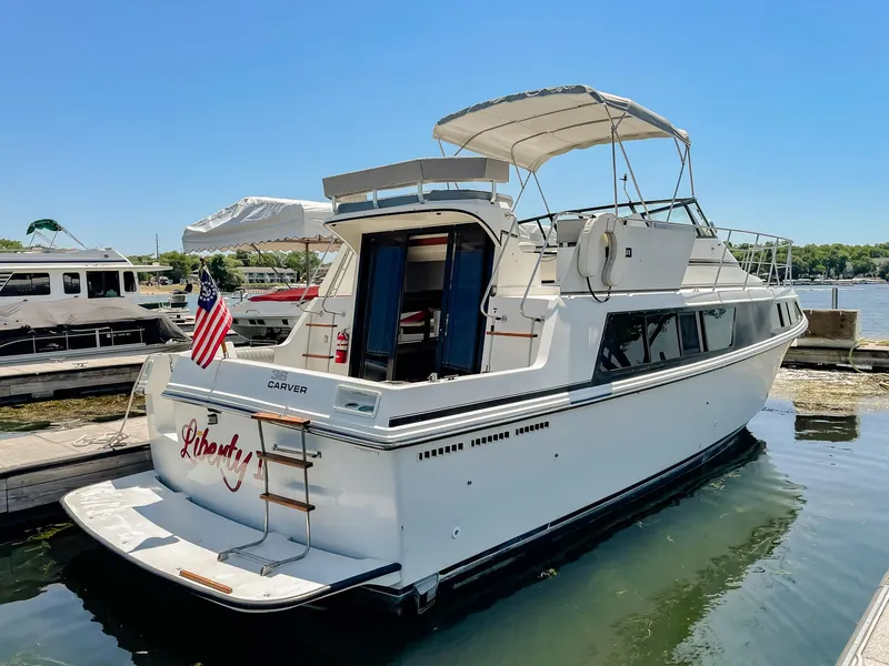 Slide: The Image of 1987 Carver 3697 Mariner yacht docked, featuring a white exterior and American flag. - 3