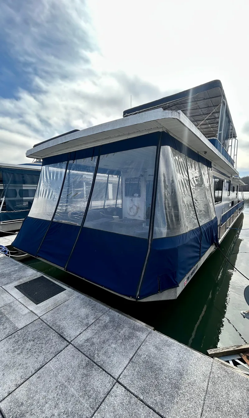 Slide: The Image of 1987 Jamestowner houseboat docked, featuring blue and white exterior with clear panels. - 2