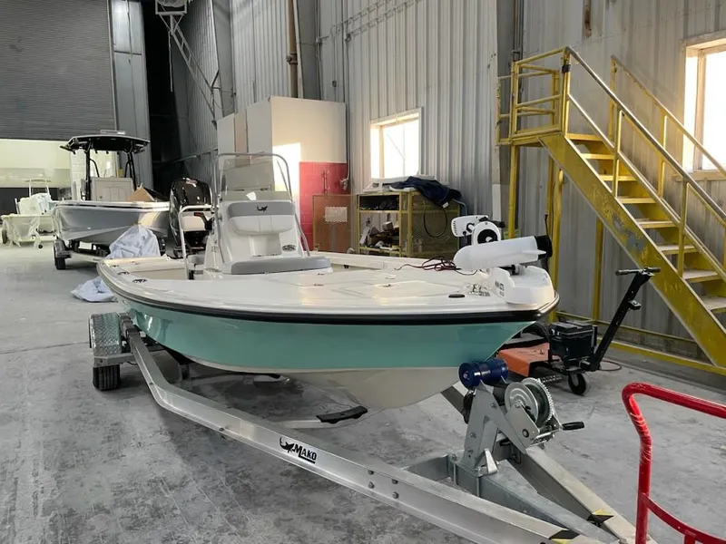 Slide: The Image of 2024 Mako 18 LTS boat in a warehouse, on a trailer, with yellow stairs nearby. - 2