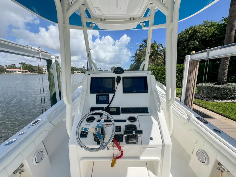 Slide: The Image of 2019 Regulator 25 boat cockpit with dual screens and steering wheel, docked by a scenic waterfront. - 17