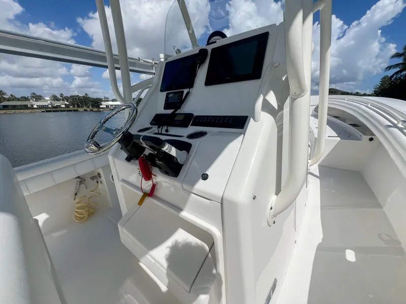 Slide: The Image of 2019 Regulator 25 boat console with steering wheel and navigation screens, docked by a lake. - 18