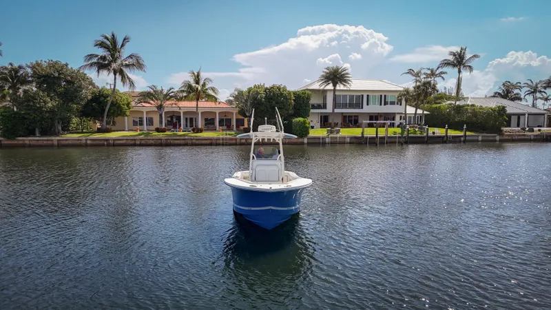 Slide: The Image of 2019 Regulator 25 boat on a calm waterfront with palm trees and luxury homes. - 2