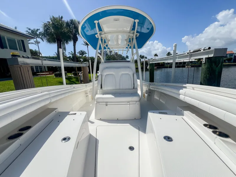 Slide: The Image of 2019 Regulator 25 boat with white seating and blue canopy, docked by waterfront homes. - 23
