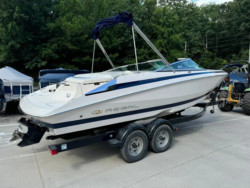 Slide: The Image of 2006 Regal 2200 Bowrider boat on trailer, parked outdoors with trees in background. - 2