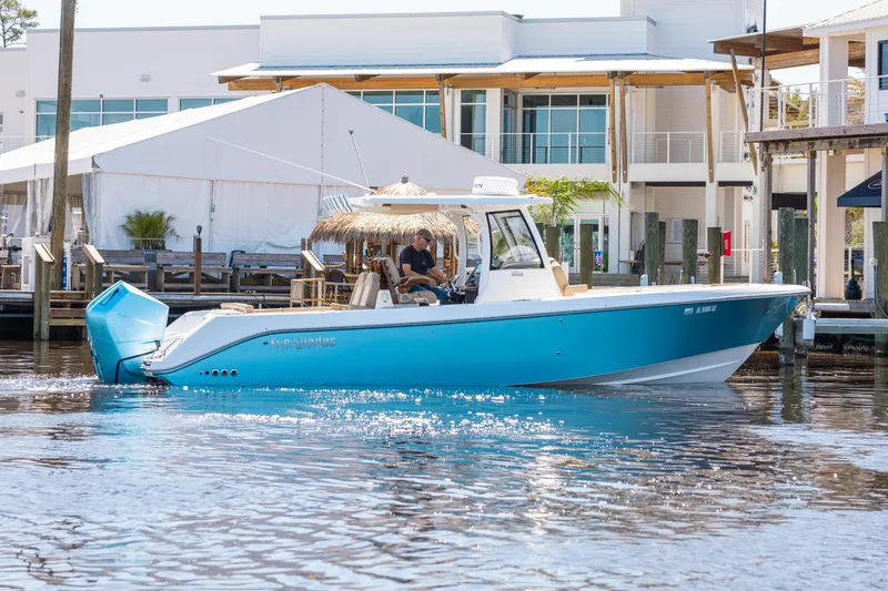 Slide: The Image of 2024 Everglades 315CC boat in marina, featuring sleek blue design and modern architecture backdrop. - 1