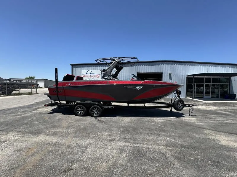 Slide: The Image of 2024 Tigé Z5 boat on trailer, parked outside a metal building under clear blue sky. - 0