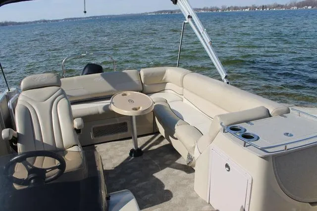 Slide: The Image of 2011 Harris 250 SL Grand Mariner pontoon boat interior with beige seating and table on a lake. - 15