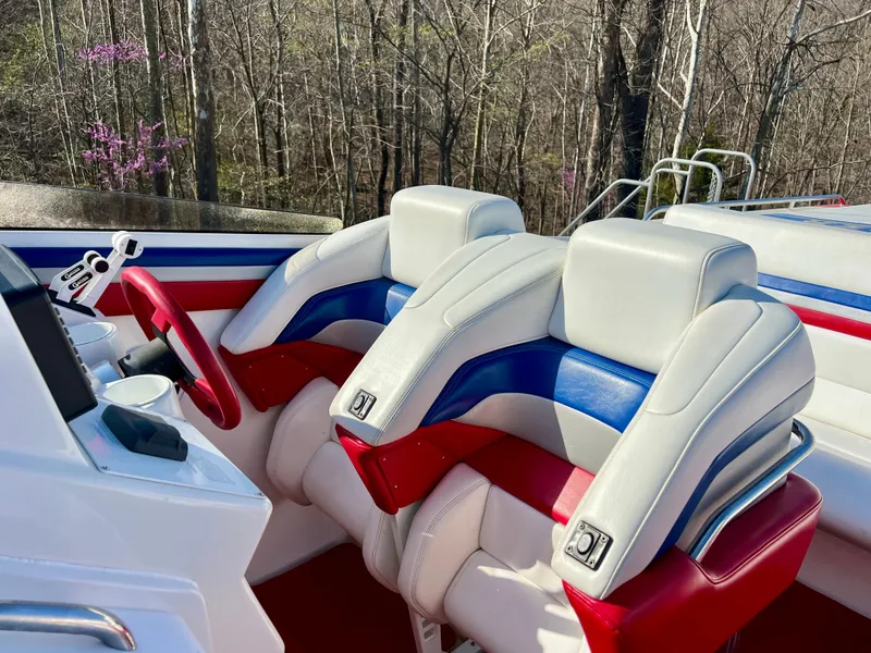 Slide: The Image of 1999 Black Thunder 430 Flat Deck boat with red, white, and blue seating, surrounded by trees. - 18