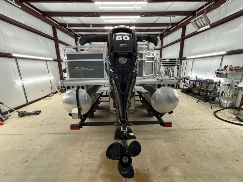 Slide: The Image of 2025 Sun Tracker Fishin Barge 20 DLX in a garage, rear view with motor. - 3