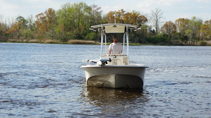 Slide: The Image of 2018 Carolina Skiff 198DLV boat cruising on a calm river with trees in the background. - 10
