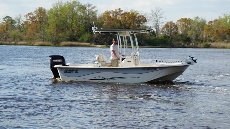 Slide: The Image of 2018 Carolina Skiff 198DLV boat cruising on a calm river with trees in the background. - 11