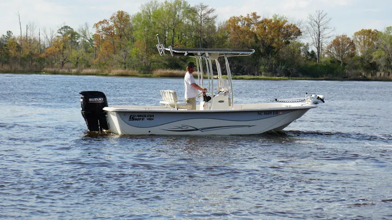 Slide: The Image of 2018 Carolina Skiff 198DLV boat cruising on a calm lake with trees in the background. - 2
