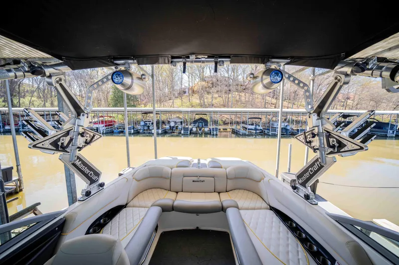 Slide: The Image of 2010 MasterCraft X25 boat interior with seating and speakers, docked by a lake. - 16