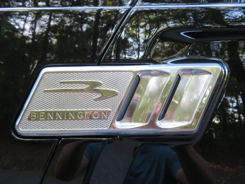 Slide: The Image of 2020 Bennington 25QXSBWAIO logo on a shiny black surface with forest reflection. - 25