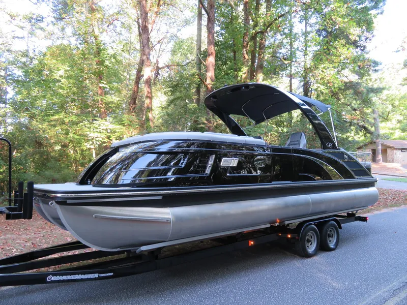 Slide: The Image of 2020 Bennington 25QXSBWAIO pontoon boat on trailer, surrounded by trees. - 4