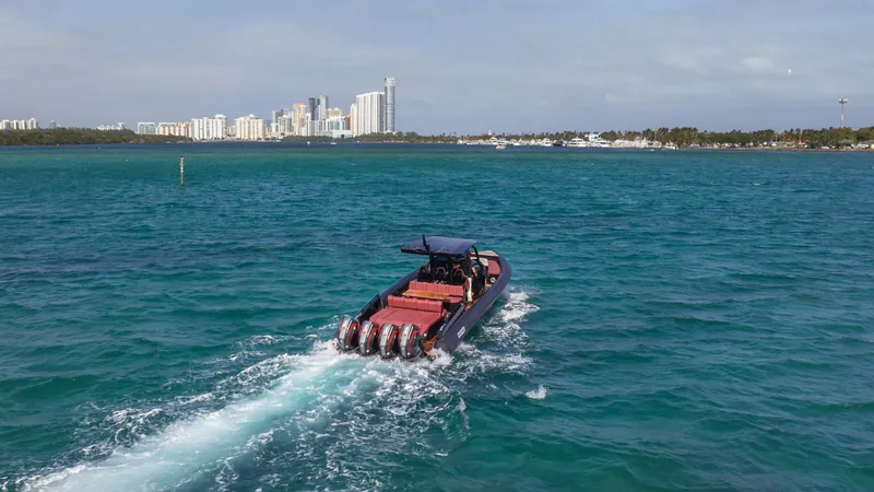 Slide: The Image of Skipper-BSK 42 boat cruising in blue waters, city skyline in background, 2023 model. - 42