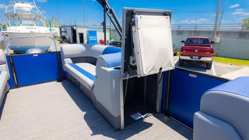 Slide: The Image of 2024 Bennington 20 SSR pontoon boat interior with blue and gray seating, docked near a red truck. - 17