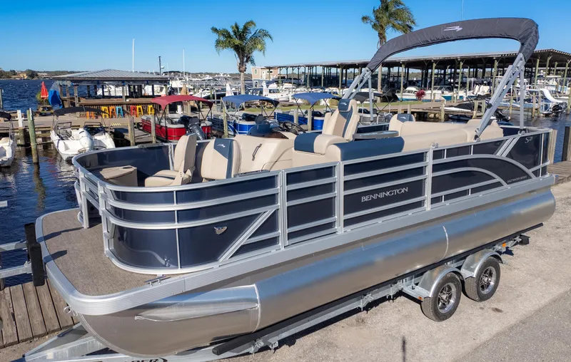 Slide: The Image of 2025 Bennington 21 SF pontoon boat docked at a marina with clear blue skies. - 2