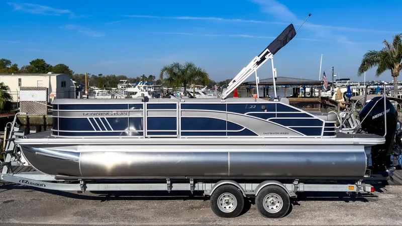 Slide: The Image of 2024 Bennington 22 LSB pontoon boat on trailer, dockside with palm trees and clear sky. - 1