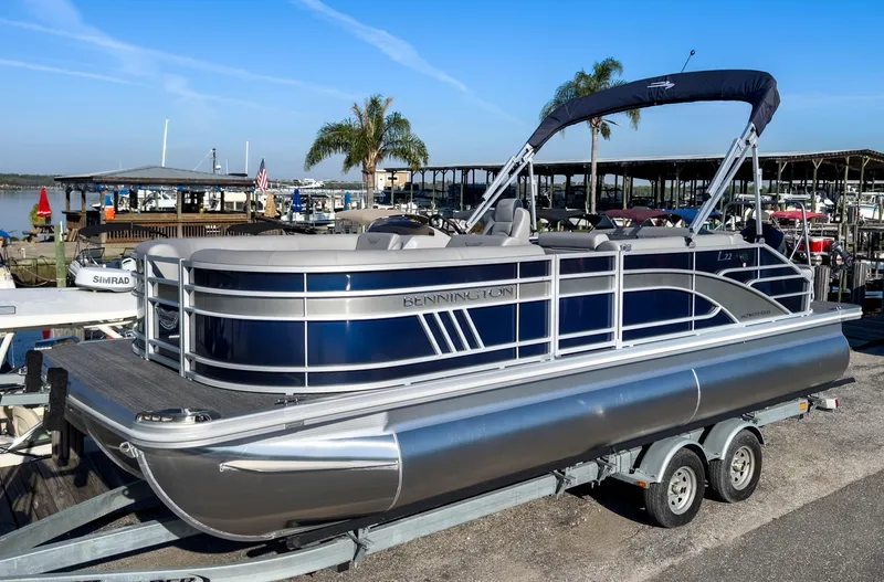 Slide: The Image of 2024 Bennington 22 LSB pontoon boat on trailer at marina, sunny day. - 2