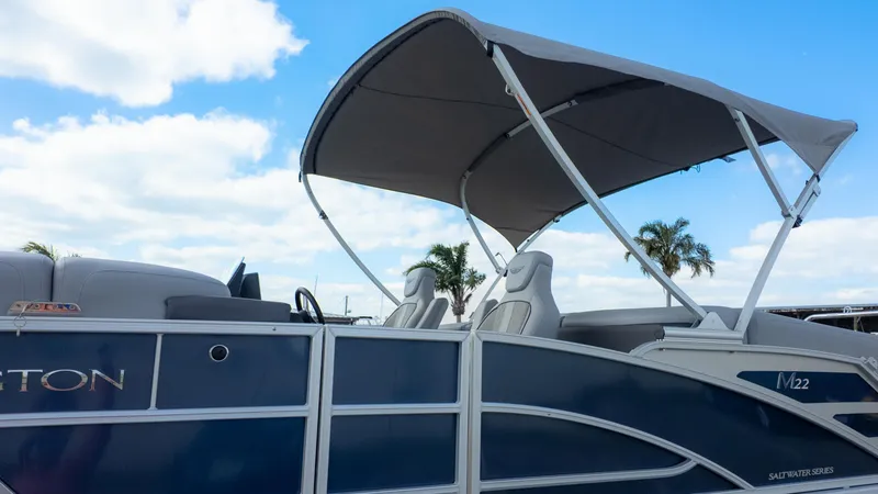 Slide: The Image of 2025 Bennington 22 MFB pontoon boat with canopy, blue exterior, and palm trees in background. - 25