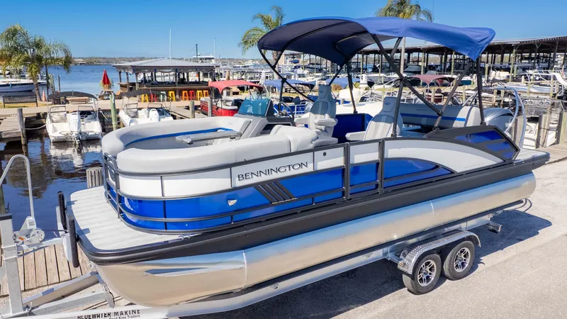 Slide: The Image of 2025 Bennington 22 MSB pontoon boat on trailer at marina, featuring blue and white design. - 2
