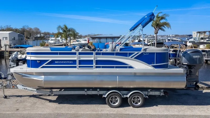 Slide: The Image of 2025 Bennington 22 SSR pontoon boat on trailer, blue and silver design, docked near marina. - 1