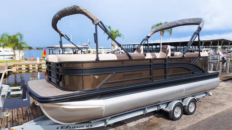 Slide: The Image of 2025 Bennington 22 SSR pontoon boat on trailer by a lakeside dock. - 2