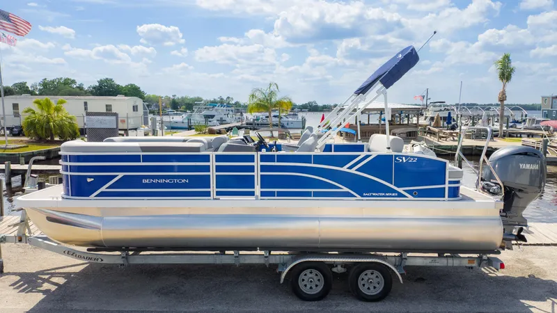Slide: The Image of 2024 Bennington 22 SVSB pontoon boat on trailer, dockside, with Yamaha outboard motor. - 2