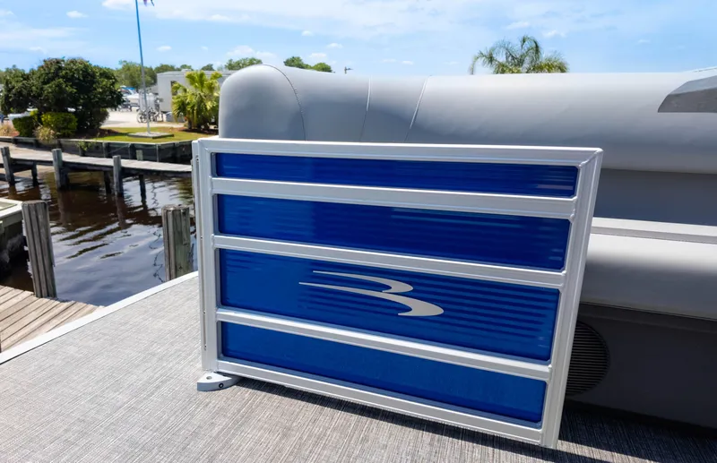 Slide: The Image of 2024 Bennington 22 SVSR pontoon boat with blue paneling, docked by a serene waterfront. - 20