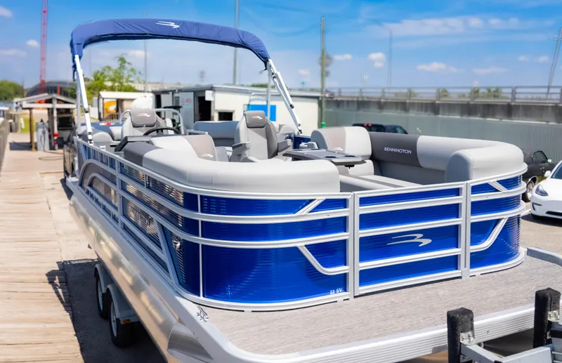 Slide: The Image of 2024 Bennington 22 SVSR pontoon boat with blue and gray design, docked under clear skies. - 3
