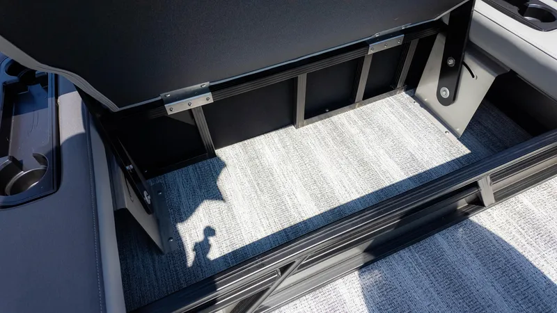 Slide: The Image of 2025 Bennington 23 SSB boat interior storage compartment with gray carpet and cup holders. - 15