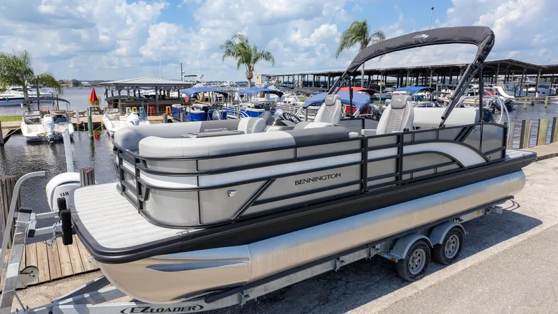Slide: The Image of 2025 Bennington 23 SSB pontoon boat on trailer at marina, under blue sky. - 2