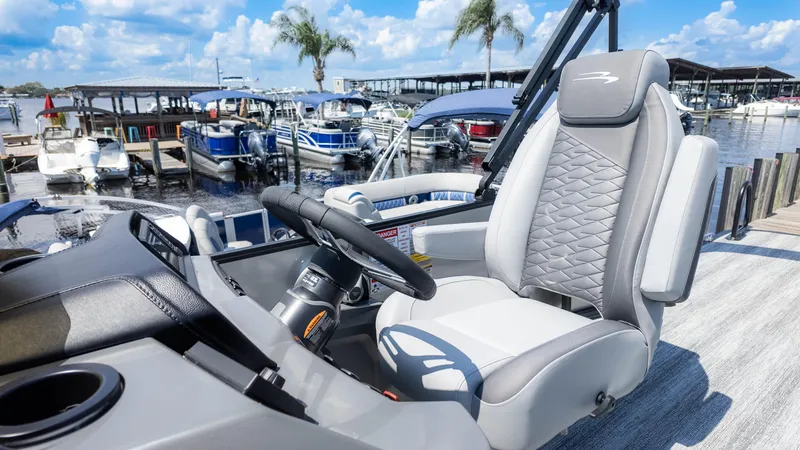 Slide: The Image of Captain's seat of 2025 Bennington 23 SSB boat at marina, with steering wheel and docked boats. - 25