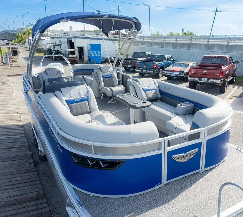 Slide: The Image of 2024 Bennington 24 LXSFBA pontoon boat with blue and gray seating, docked near trucks. - 3