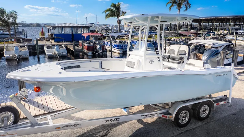 Slide: The Image of 2025 Tidewater 220cc boat on trailer at marina, clear sky, palm trees in background. - 2