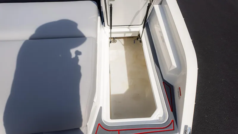 Slide: The Image of 2024 Cobalt CS23 Surf boat storage compartment with open lid and cushioned seating. - 18