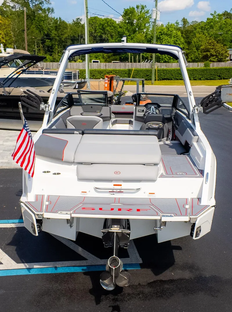 Slide: The Image of 2024 Cobalt CS23 Surf boat, rear view, with American flag, parked outdoors. - 7