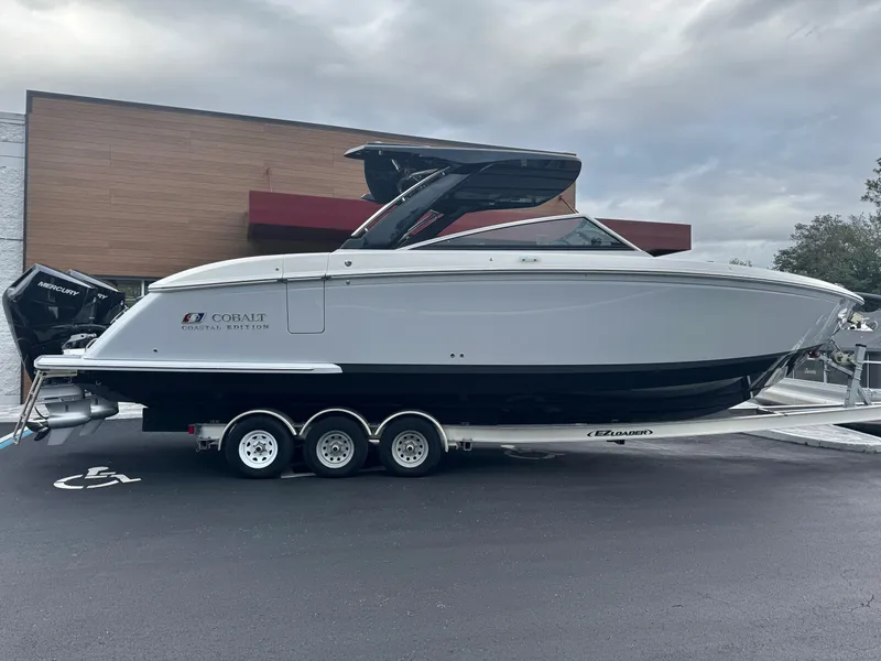Slide: The Image of 2025 Cobalt R33 boat on trailer, parked outdoors, featuring sleek design and Mercury engines. - 2