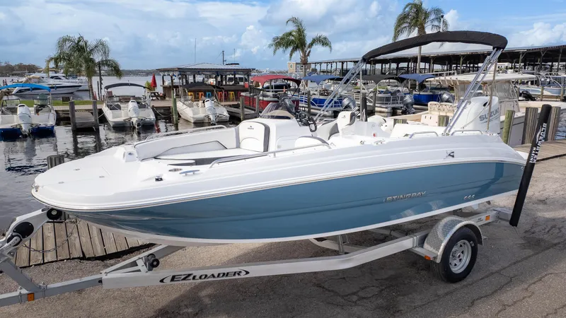 Slide: The Image of 2025 Stingray 192SC boat on trailer at marina, surrounded by other boats and palm trees. - 2