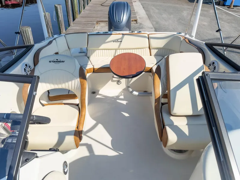 Slide: The Image of 2024 Stingray 211DC boat interior with beige seating and wooden table, docked at marina. - 13