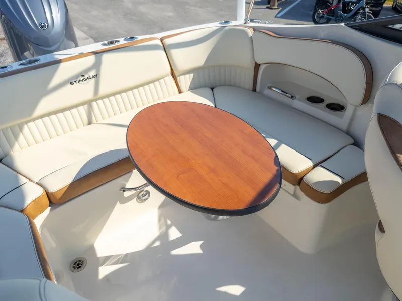 Slide: The Image of 2024 Stingray 211DC boat interior with beige seating and wooden table. - 18