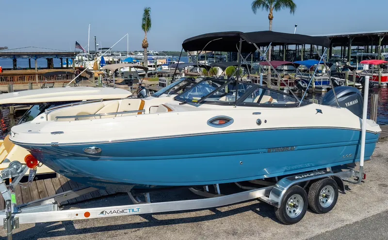 Slide: The Image of 2024 Stingray 211DC boat on trailer at marina, featuring blue and white design. - 4