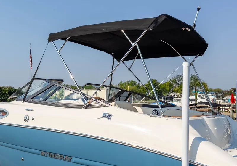 Slide: The Image of 2024 Stingray 211DC boat with canopy, docked at marina under clear sky. - 8