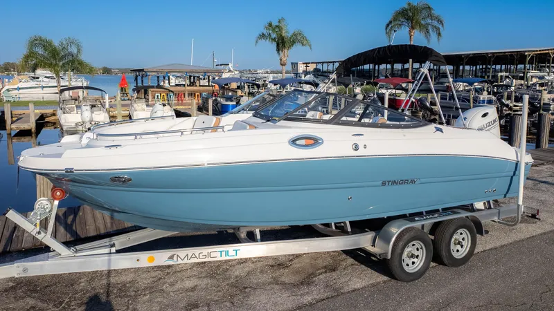 Slide: The Image of 2025 Stingray 231DC boat on trailer at marina, surrounded by palm trees and water. - 2