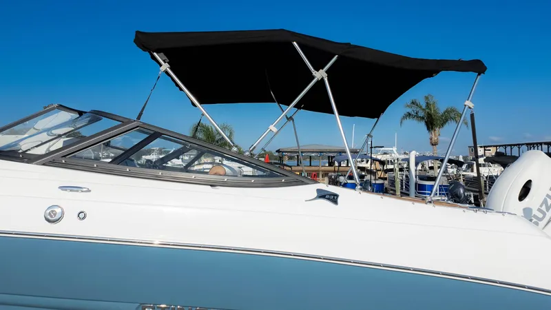 Slide: The Image of 2025 Stingray 231DC boat with black canopy, docked at marina under clear blue sky. - 31